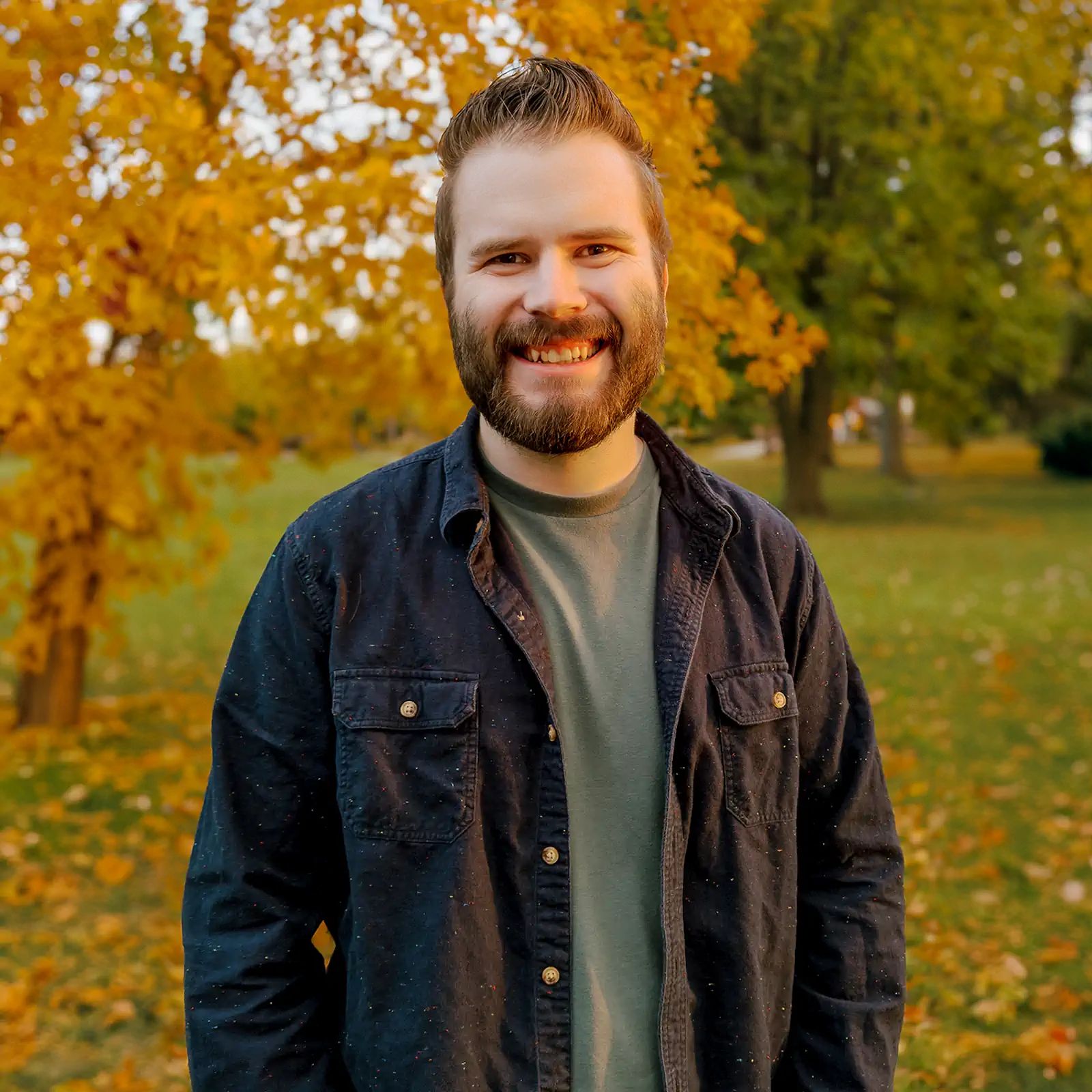 Connor smiling in front of an out of focus tree turning yellow and losing leaves with warm evening sunlight falling across his face